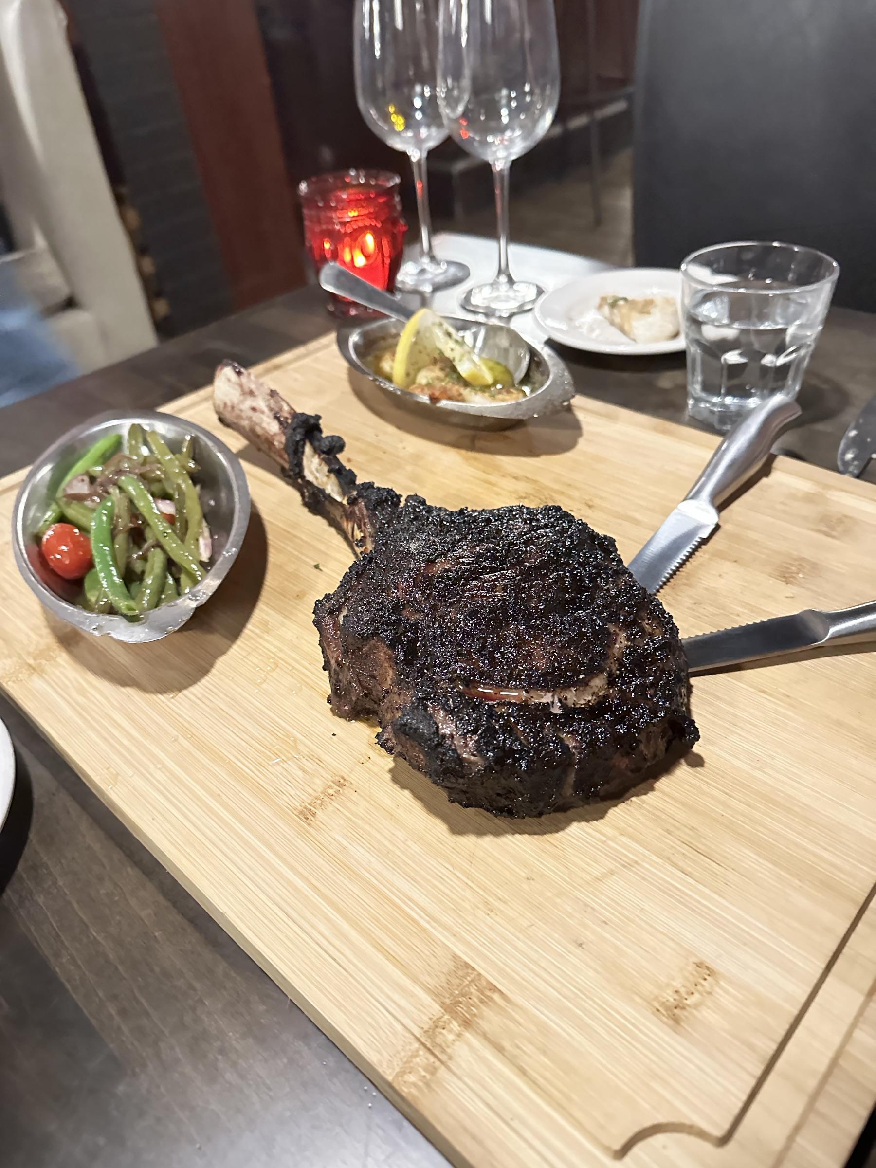 Bone-in ribeye on a butcher block, candlelight in the background.