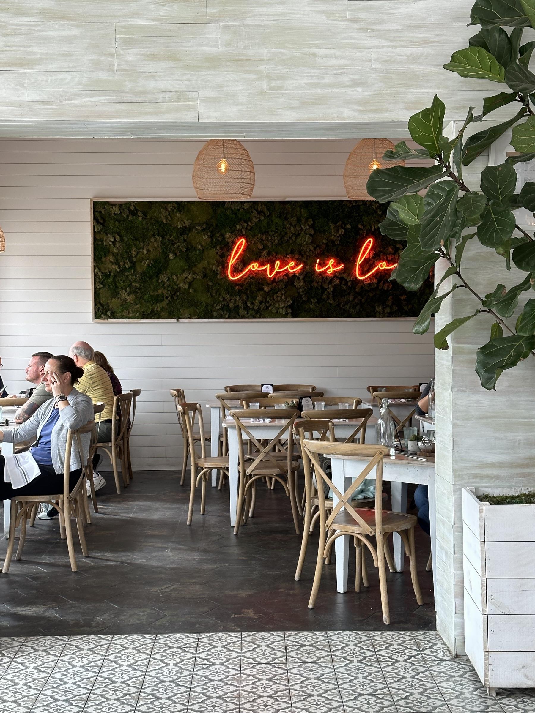 Whitewashed cafe interior with a “love is love” neon sign.