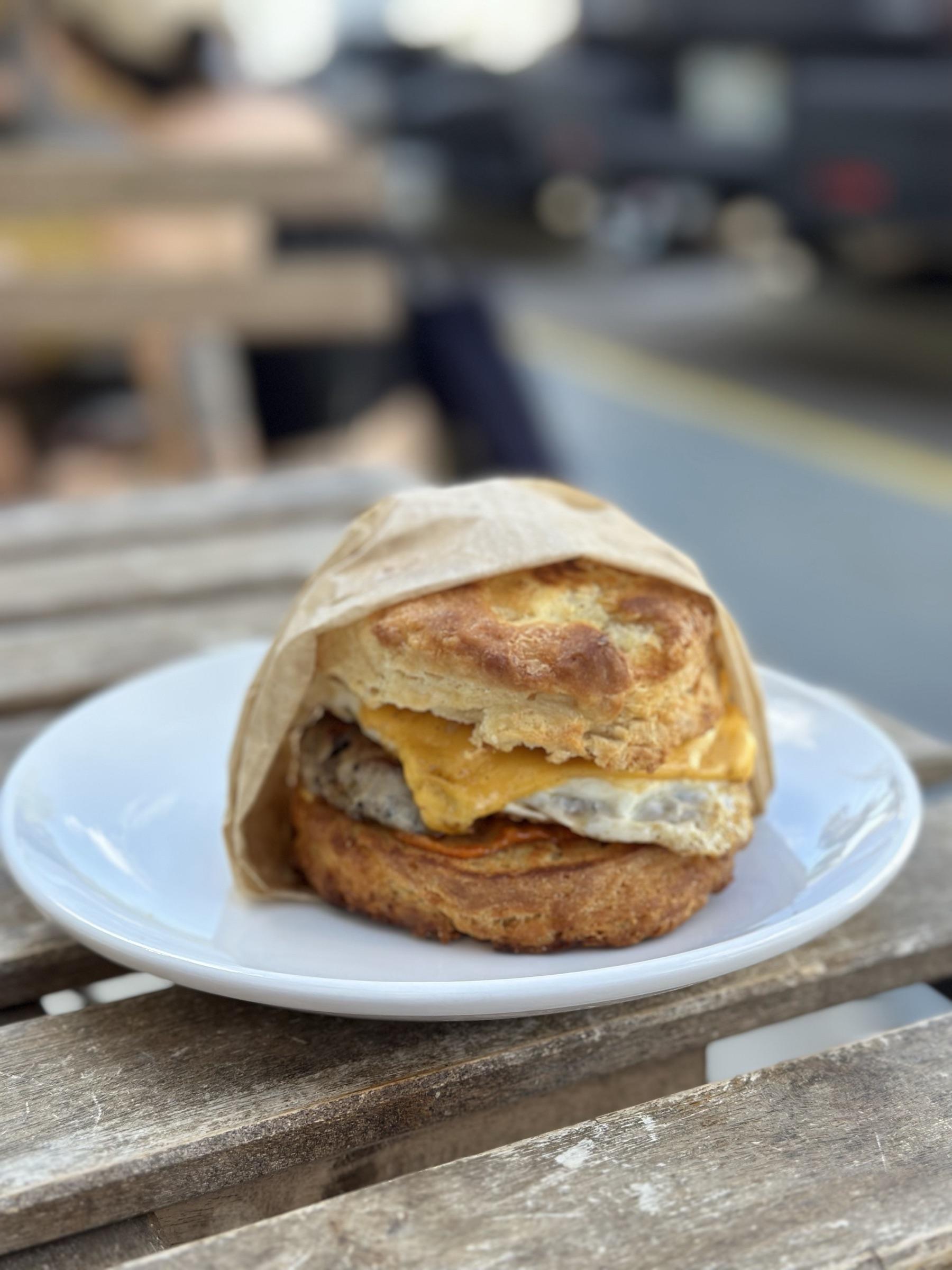 A breakfast biscuit sandwich on a picnic table outside a food truck.