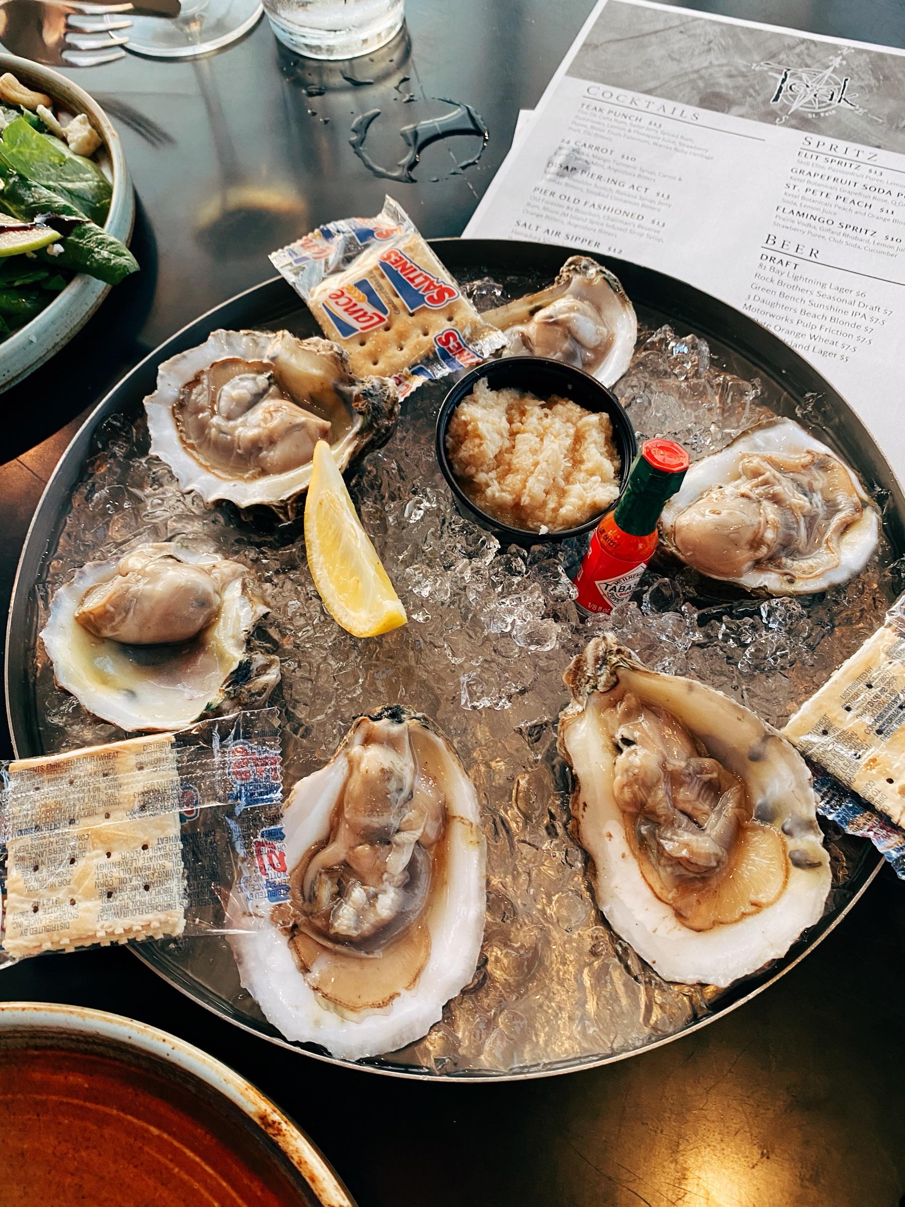 A platter of raw oysters on ice with crackers and Crystal hot sauce.