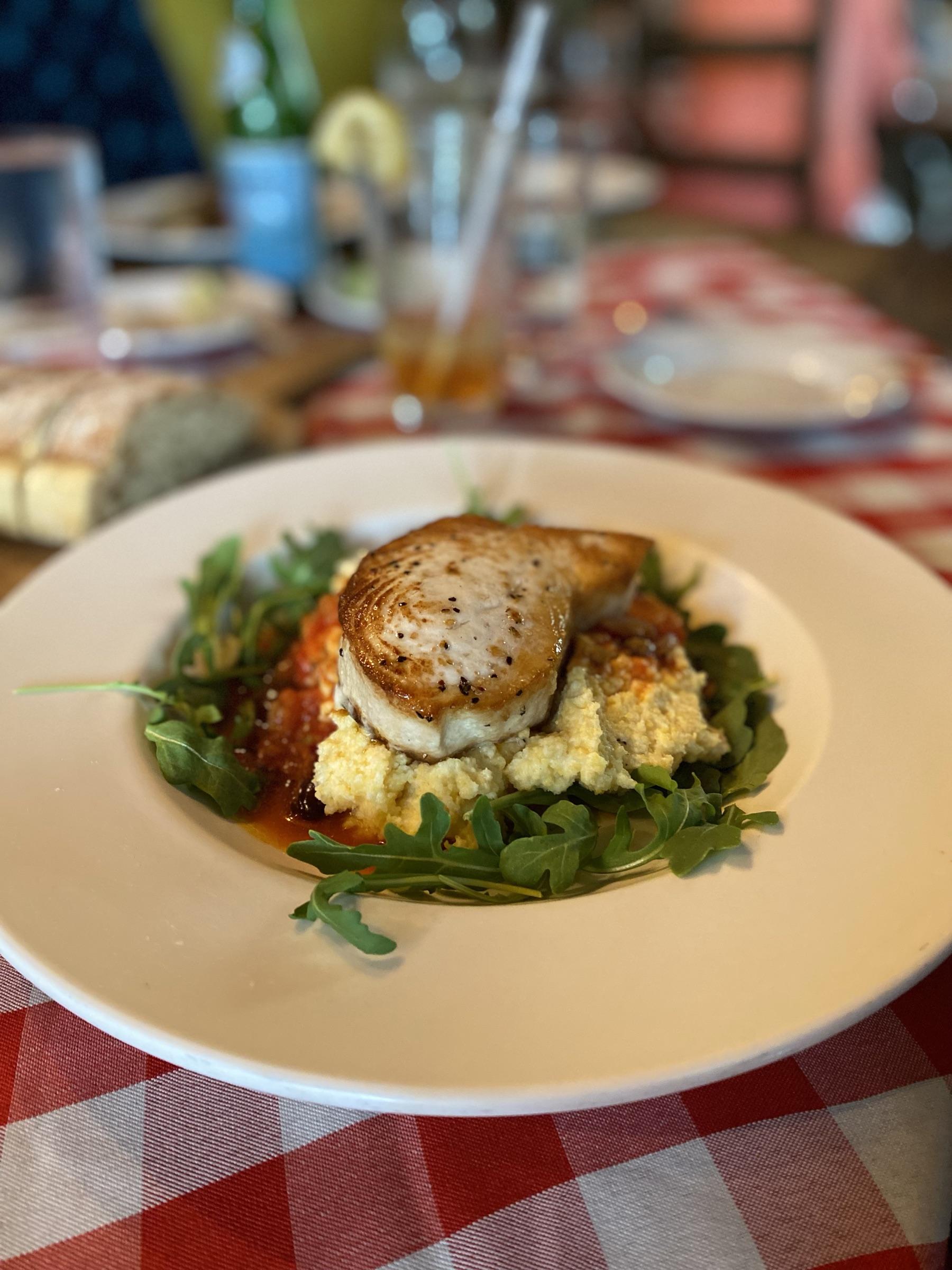 Seared swordfish over polenta and arugula on a checked tablecloth.
